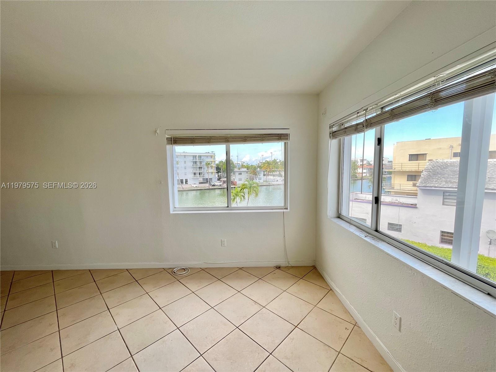 An empty room with beige tile flooring and two windows overlooking a canal — 1185 Marseille Dr # 309, Miami Beach FL 33141, MIAMI BEACH, FL