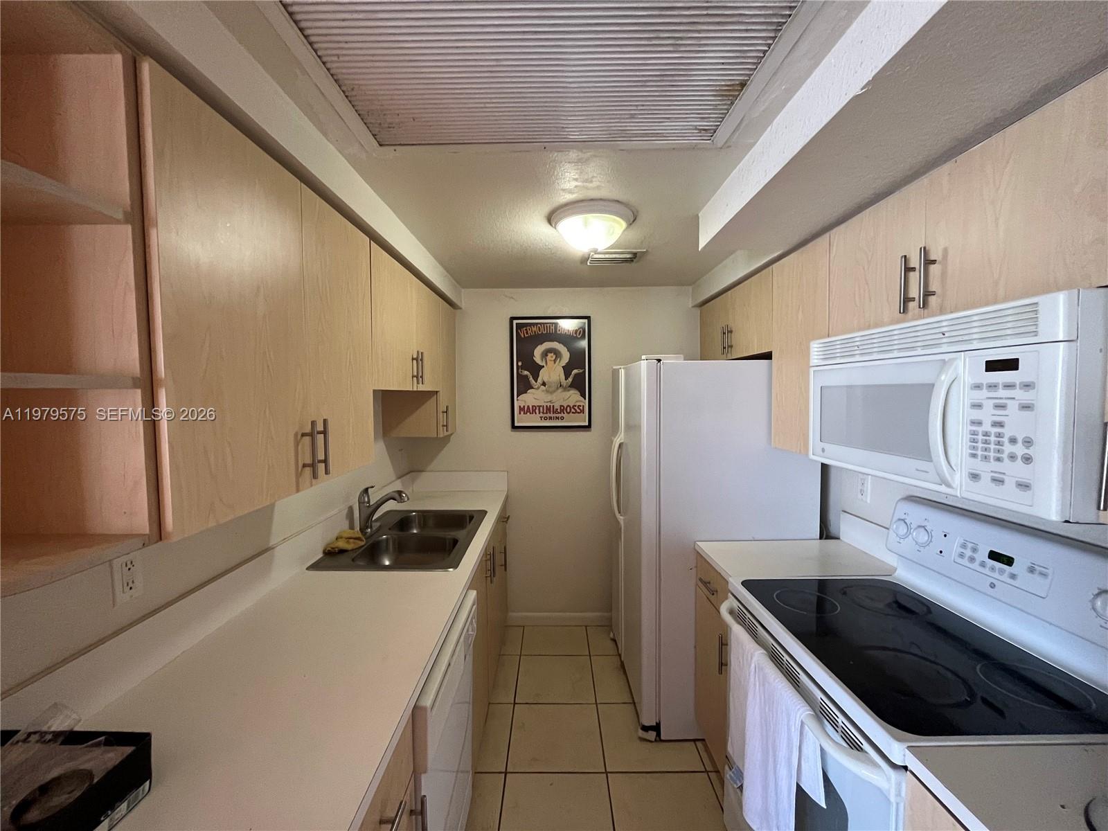 A galley-style kitchen features light wood cabinets, white countertops, and white appliances — 1185 Marseille Dr # 309, Miami Beach FL 33141, MIAMI BEACH, FL