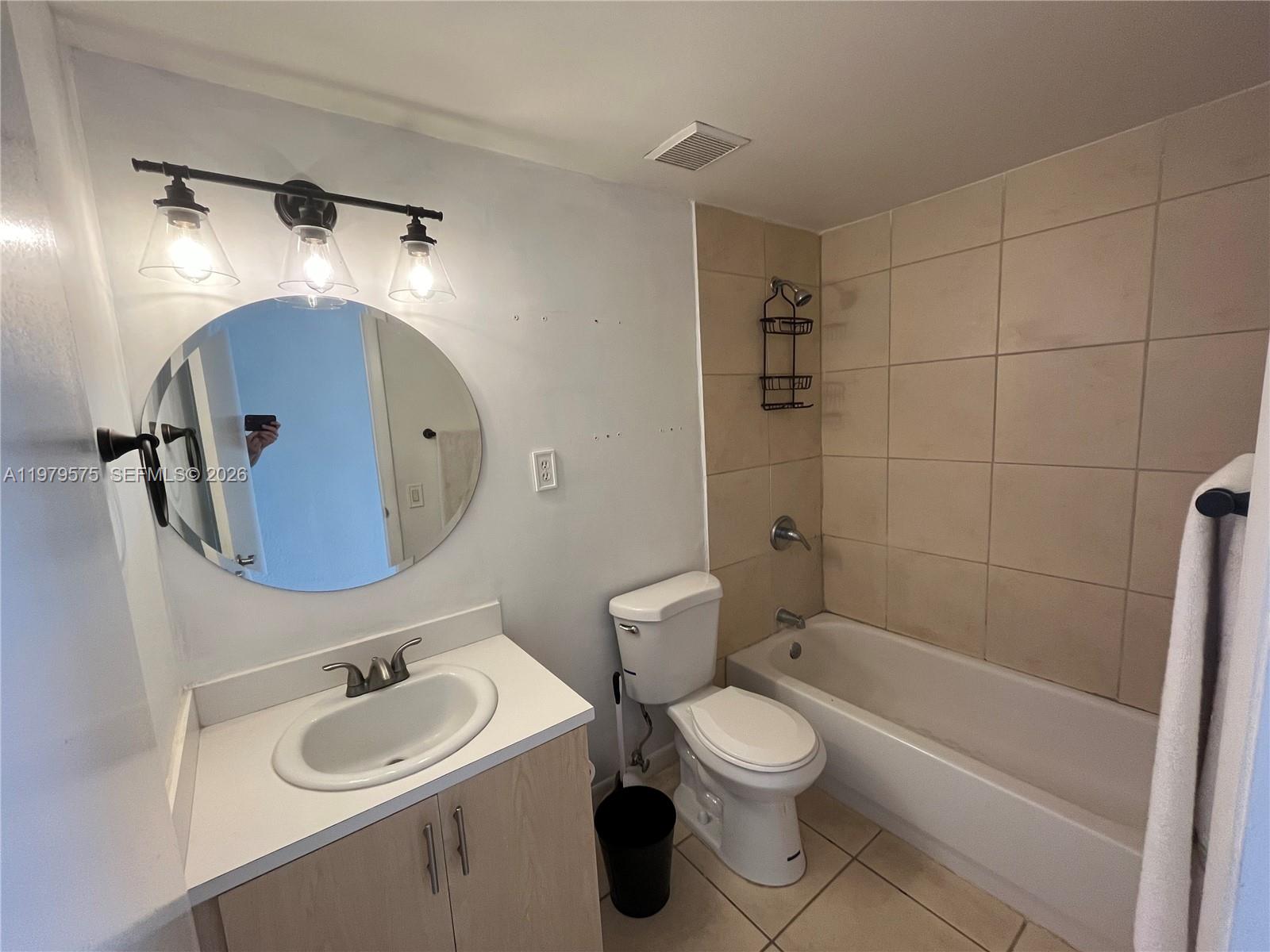 A bathroom features a vanity with a round mirror, a toilet, and a tiled bathtub — 1185 Marseille Dr # 309, Miami Beach FL 33141, MIAMI BEACH, FL