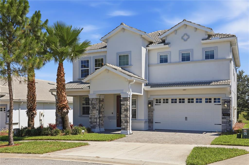 A two-story suburban house with a stone-accented entryway, white stucco exterior, and a two-car garage — 1463 BUNKER DRIVE, DAVENPORT, FL