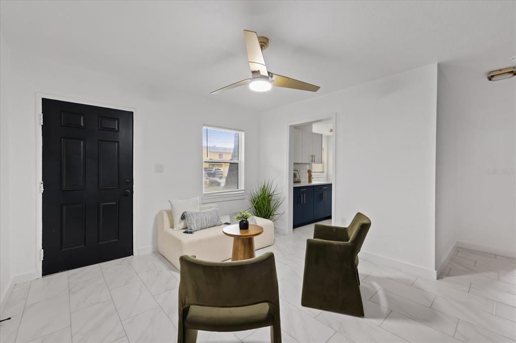 A room with white tile floors, a black door, two olive chairs, and a small sofa — 8730 N CALDER PLACE, TAMPA, FL