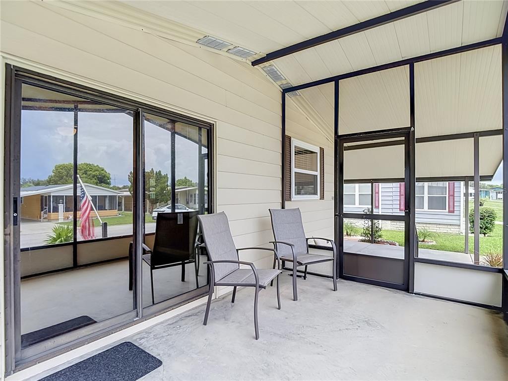 A screened-in porch features a concrete floor, two chairs, and a sliding glass door — 4919 BLANCO DRIVE, ZEPHYRHILLS, FL