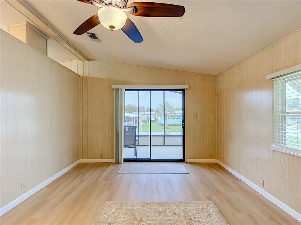 A living room with wood-paneled walls, light wood flooring, a ceiling fan, and sliding glass doors — 4919 BLANCO DRIVE, ZEPHYRHILLS, FL