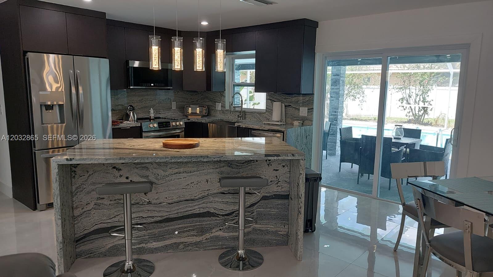 A kitchen features dark cabinets, a waterfall granite island, and a sliding door to a patio — 320 SE 15 PL, Cape Coral FL 33990, CAPE CORAL, FL