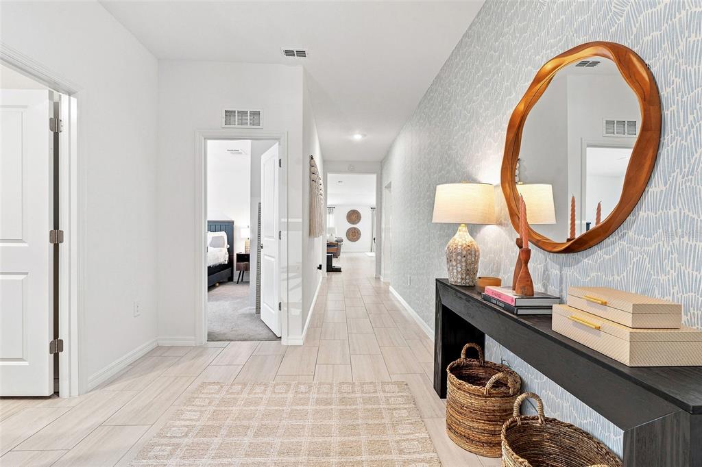 A hallway features light-colored tile flooring, patterned wallpaper, a console table, and a round mirror — 15173 RAINBOW QUARTZ STREET, WIMAUMA, FL