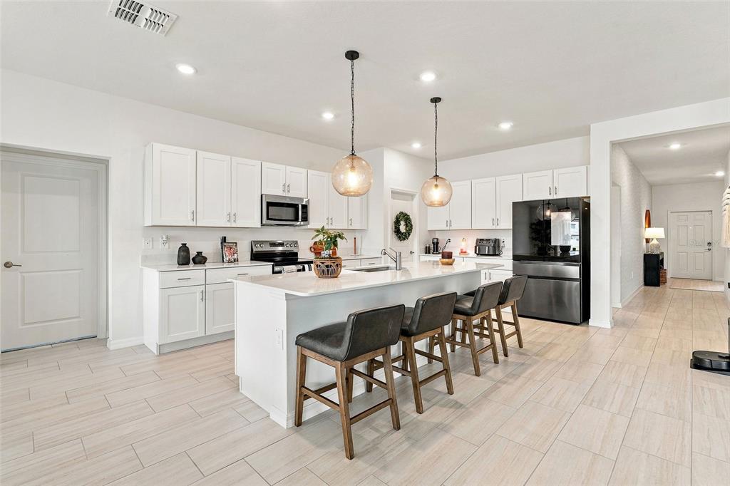 A modern kitchen features white cabinetry, a central island with bar seating, and stainless appliances — 15173 RAINBOW QUARTZ STREET, WIMAUMA, FL