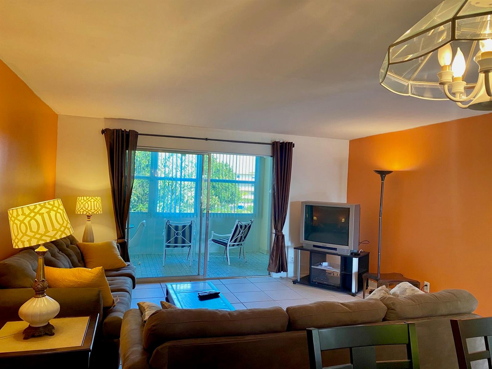 A living room with orange walls, brown sofas, a television, and a sliding glass balcony door — 2615 NE 3rd Court # 302, Boynton Beach FL 33435, BOYNTON BEACH, FL