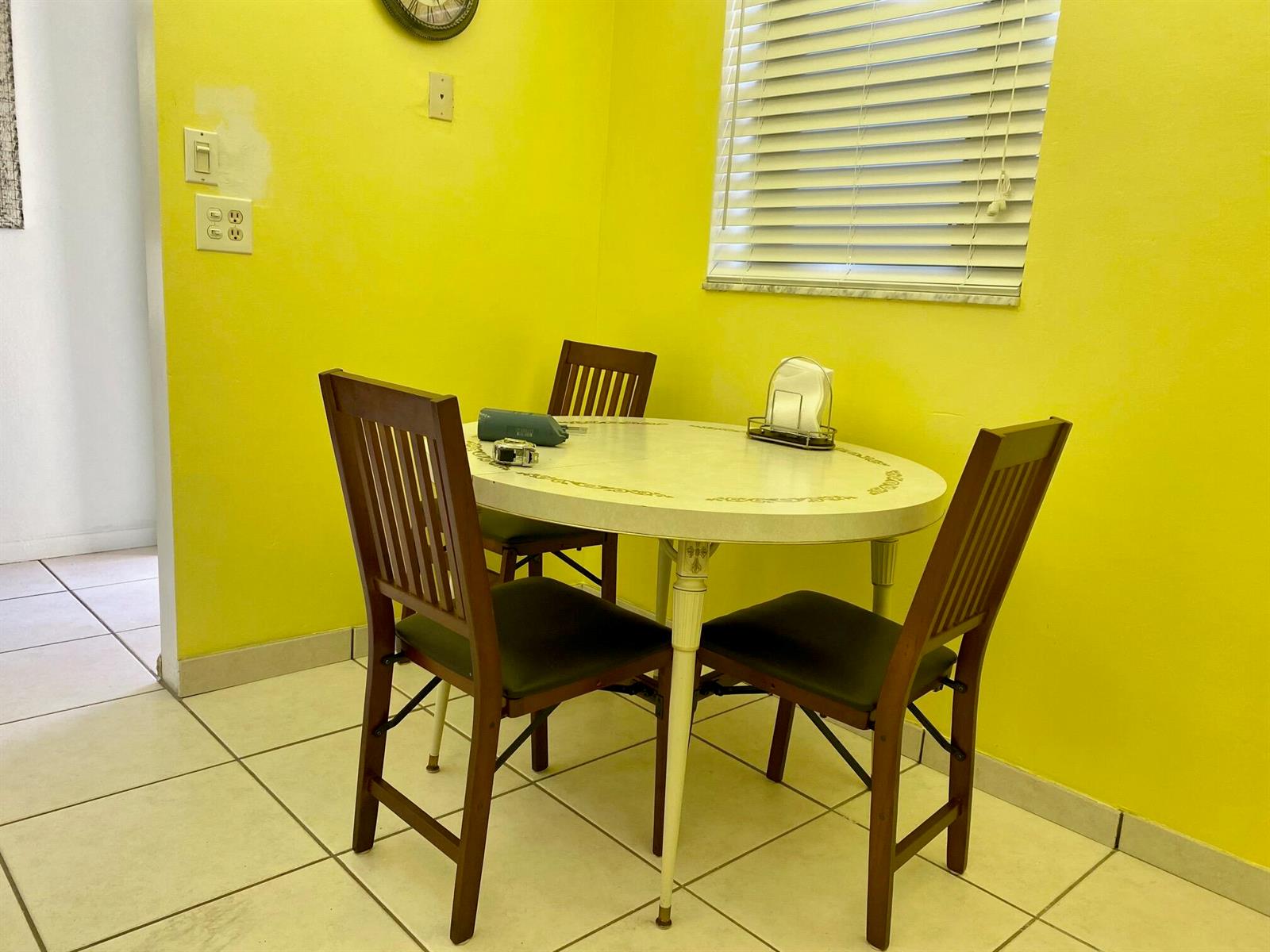 A dining area features a round table with three wooden chairs against bright yellow walls — 2615 NE 3rd Court # 302, Boynton Beach FL 33435, BOYNTON BEACH, FL