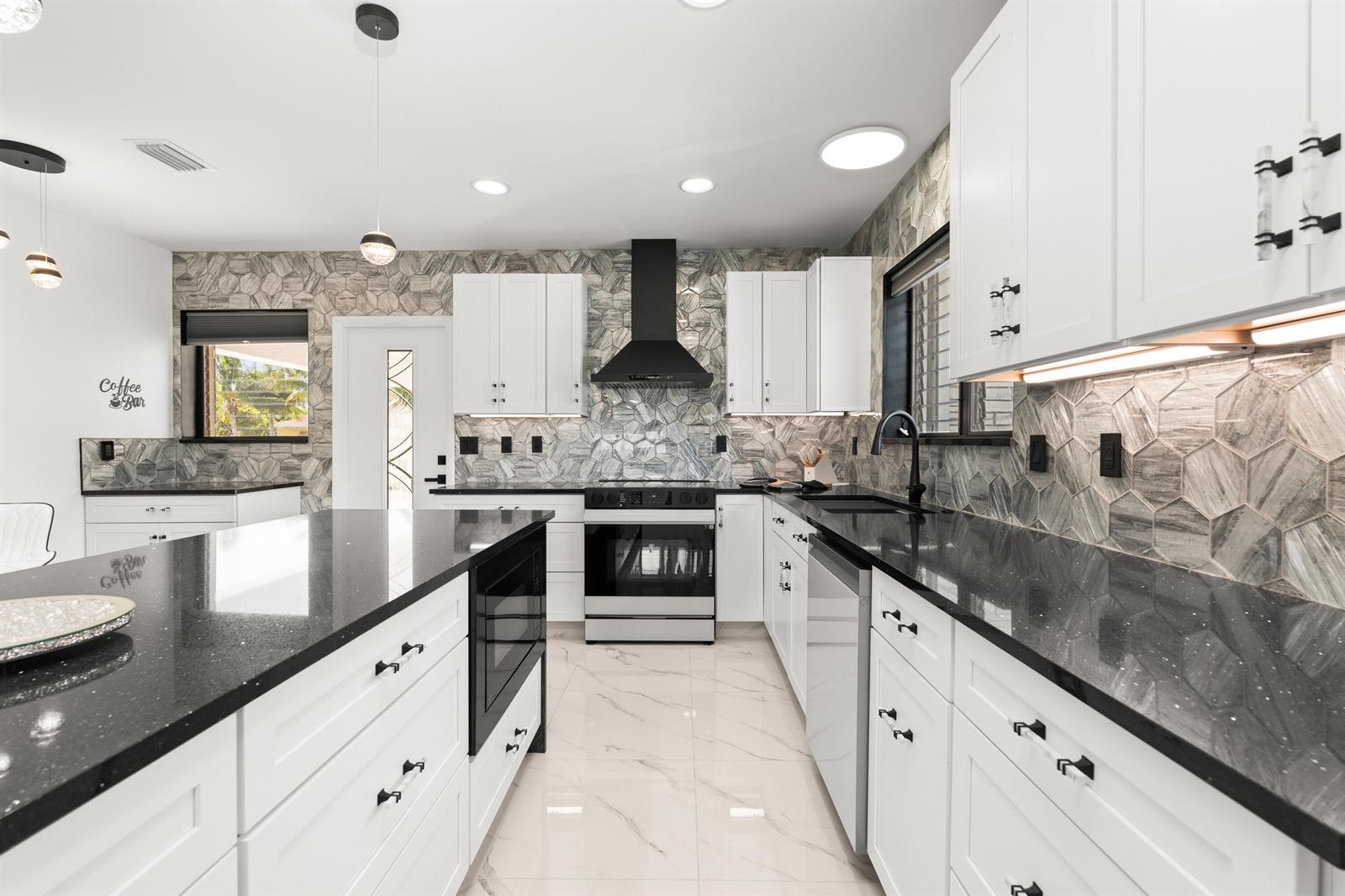 A modern kitchen features white cabinets, black countertops, a hexagonal tile backsplash, and stainless appliances — 1428 N M Street, Lake Worth FL 33460, LAKE WORTH, FL
