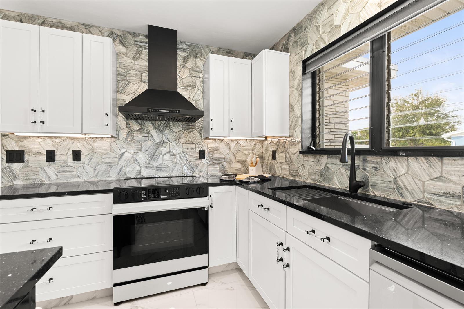 A kitchen features white cabinets, black countertops, a black range hood, and hexagonal patterned backsplash tiles — 1428 N M Street, Lake Worth FL 33460, LAKE WORTH, FL