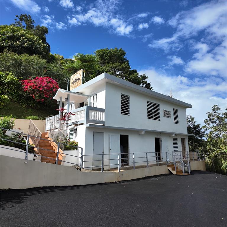 A two-story white house with a balcony and outdoor stairs sits on a paved lot — Carr 157 KM 23.2 INT BO. BARROS, OROCOVIS, PR