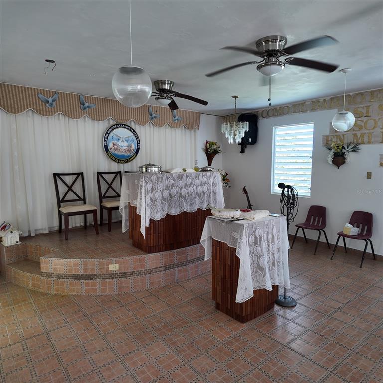 A small church sanctuary features a raised altar, tiled floors, ceiling fans, and wooden podiums — Carr 157 KM 23.2 INT BO. BARROS, OROCOVIS, PR