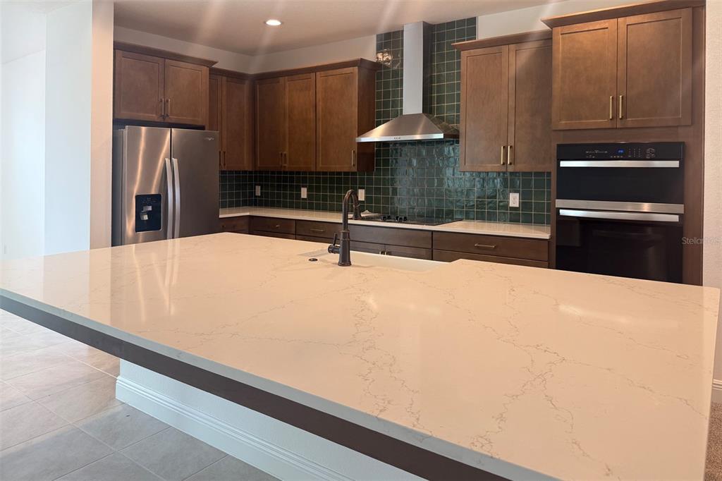 A kitchen features a large quartz island, dark wood cabinets, and a green tiled backsplash — 2029 HEART LAKE DRIVE, GROVELAND, FL