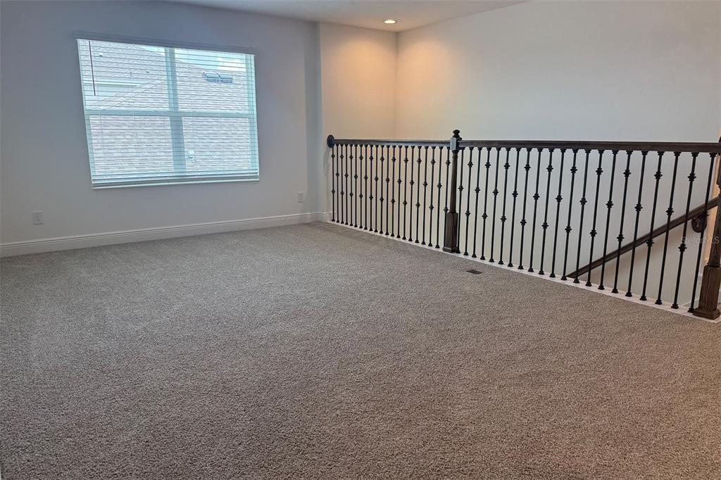 An upstairs carpeted loft features a window with blinds and a dark metal stair railing — 2029 HEART LAKE DRIVE, GROVELAND, FL