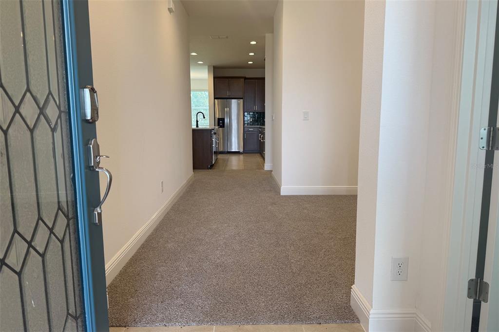 A view from an entryway looking down a carpeted hallway toward a kitchen with cabinets — 2029 HEART LAKE DRIVE, GROVELAND, FL