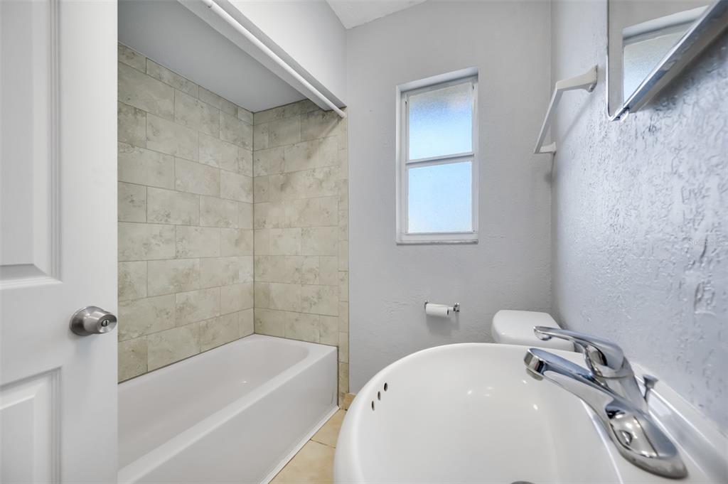 A bathroom features a tiled bathtub surround, a white pedestal sink, and a small window — 1070 S CLEARVIEW AVE UNIT 10, TAMPA, FL