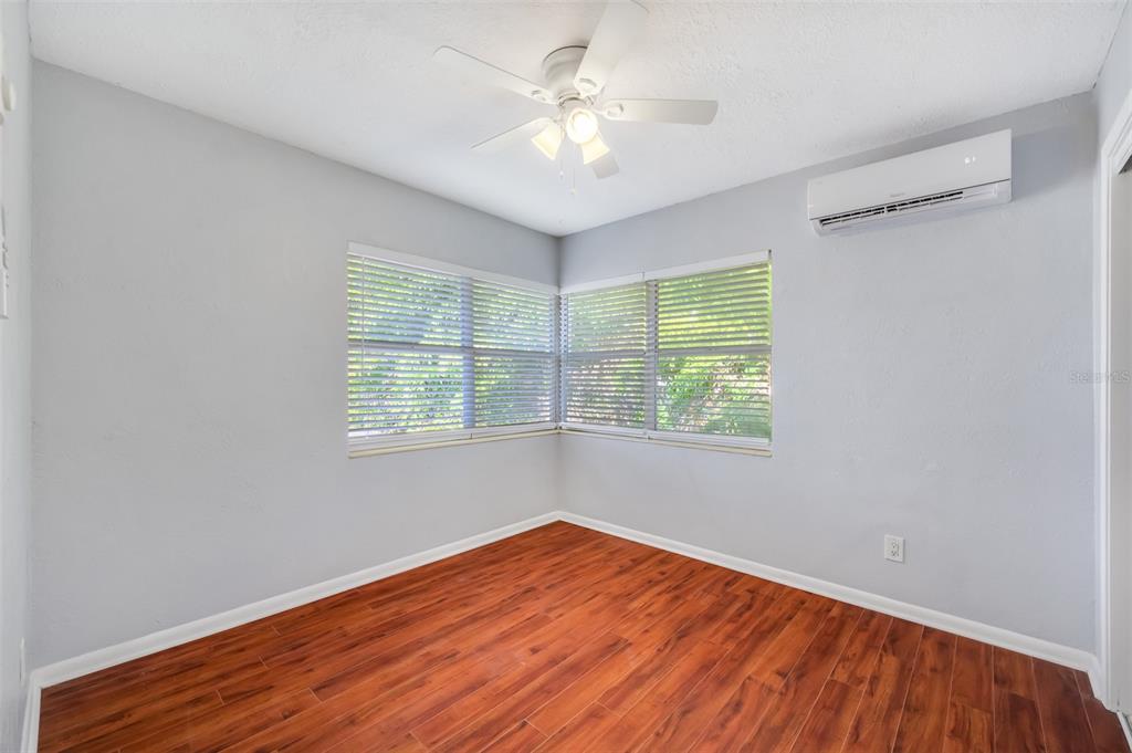 An empty room with light gray walls, wood-look flooring, a ceiling fan, and wall-mounted AC — 1070 S CLEARVIEW AVE UNIT 10, TAMPA, FL