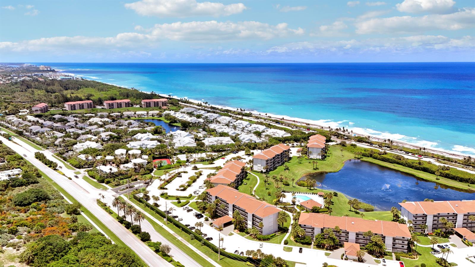 An aerial view shows a coastal resort complex with multiple buildings, a pond, and beach — 401 S Seas Drive # 203, Jupiter FL 33477, JUPITER, FL