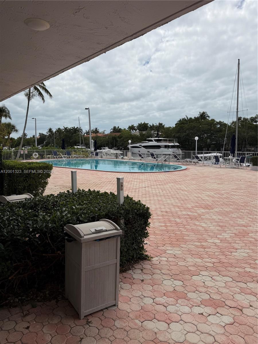 A swimming pool sits on a paved patio overlooking a marina with docked yachts — 100 Edgewater Dr # 127, Coral Gables FL 33133, CORAL GABLES, FL
