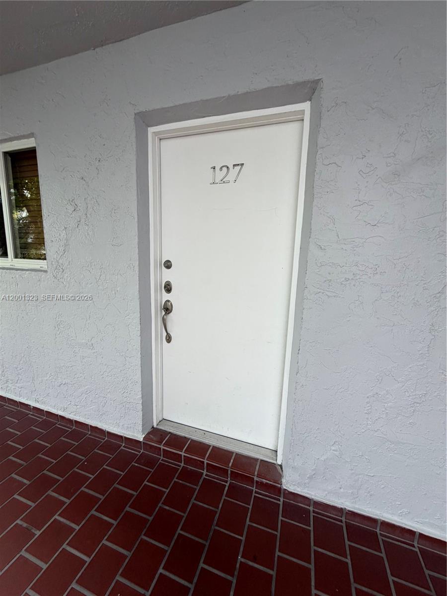 A white door marked 127 is set into a gray stucco wall above a tiled patio — 100 Edgewater Dr # 127, Coral Gables FL 33133, CORAL GABLES, FL