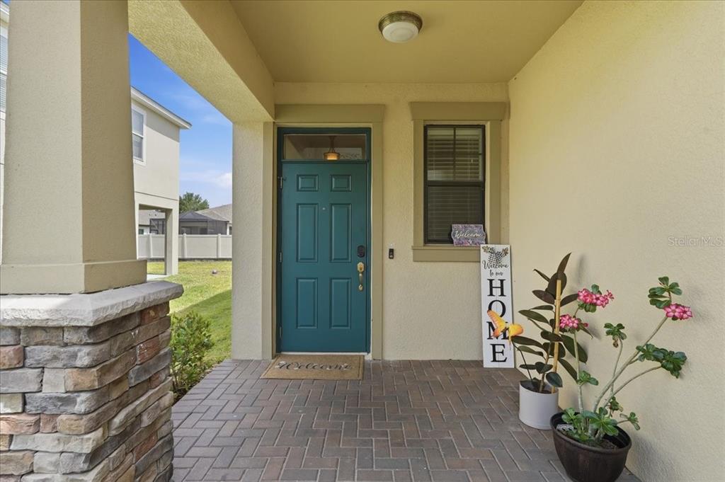A covered front porch features a teal door, brick pavers, and a potted plant — 1020 OLIVETO VERDI COURT, BRANDON, FL