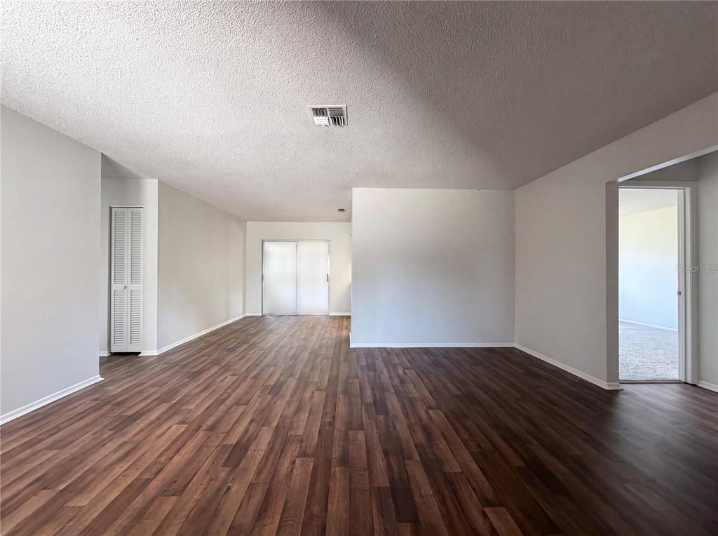 An empty living room features wood-look flooring, white walls, and a sliding glass door — 607 33RD AVENUE DRIVE E, BRADENTON, FL