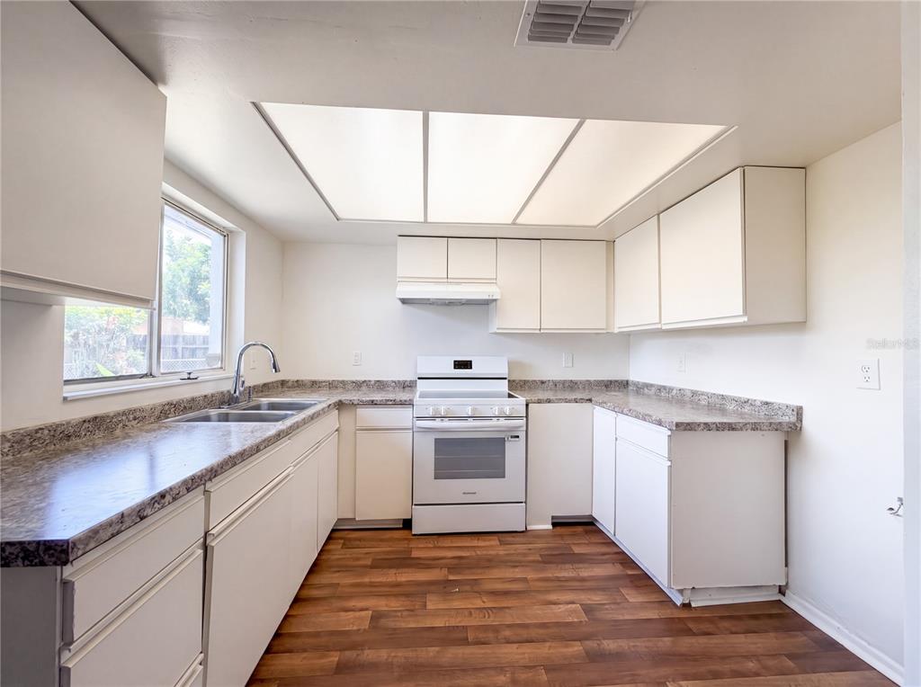 A kitchen with white cabinets, laminate countertops, a white stove, and wood-look flooring — 607 33RD AVENUE DRIVE E, BRADENTON, FL