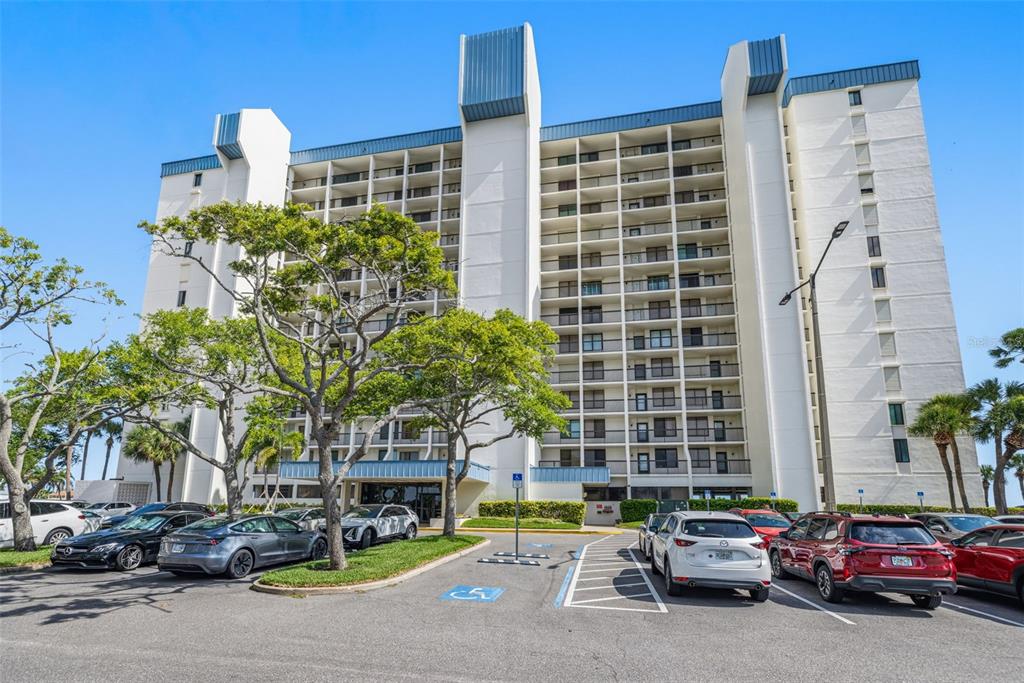 A multi-story white apartment building with balconies stands behind a paved parking lot — 9495 BLIND PASS ROAD UNIT 206, ST PETE BEACH, FL