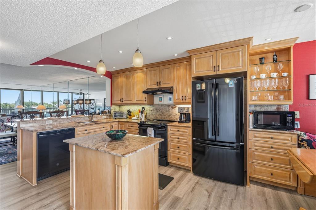 A kitchen features light wood cabinetry, granite countertops, black appliances, and an island — 9495 BLIND PASS ROAD UNIT 206, ST PETE BEACH, FL