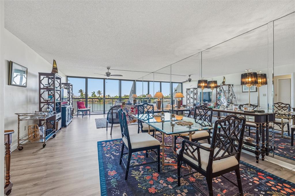 A dining area with a glass table and mirrored wall overlooks a balcony and water view — 9495 BLIND PASS ROAD UNIT 206, ST PETE BEACH, FL
