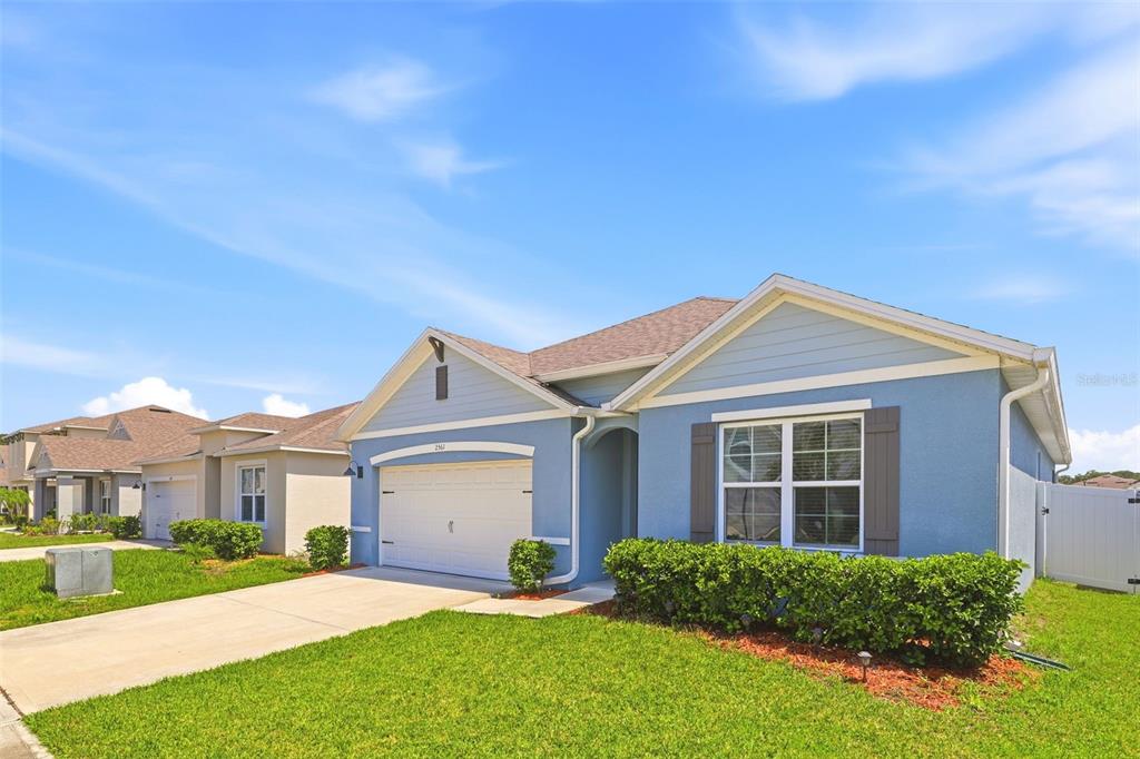 A blue single-story suburban house features a two-car garage, a front lawn, and landscaping — 2561 HARMONIA HAMMOCK RD, HARMONY, FL