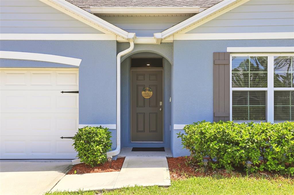 The exterior of a blue house features a front door, garage, and landscaped bushes — 2561 HARMONIA HAMMOCK RD, HARMONY, FL