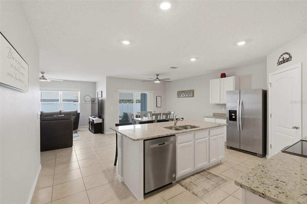 A kitchen with a granite island, stainless steel appliances, and white cabinets opens to a living area — 2561 HARMONIA HAMMOCK RD, HARMONY, FL