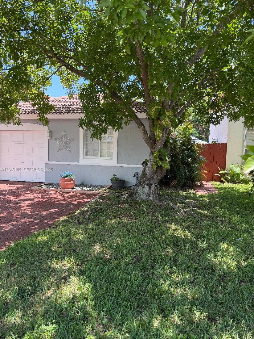 A gray house exterior features a white garage door, a star decoration, and a large tree — 19554 NW 79th Pl, Hialeah FL 33015, HIALEAH, FL