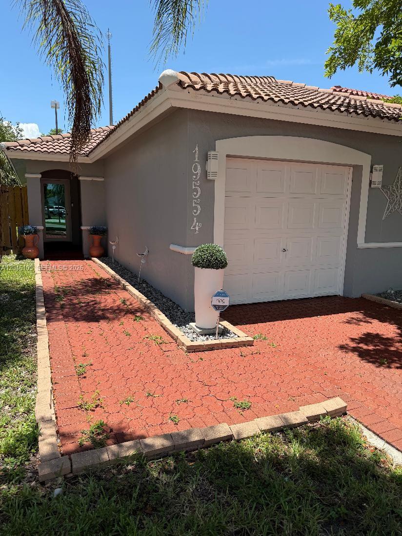 A gray house exterior features a white garage door, a red brick walkway, and landscaping — 19554 NW 79th Pl, Hialeah FL 33015, HIALEAH, FL