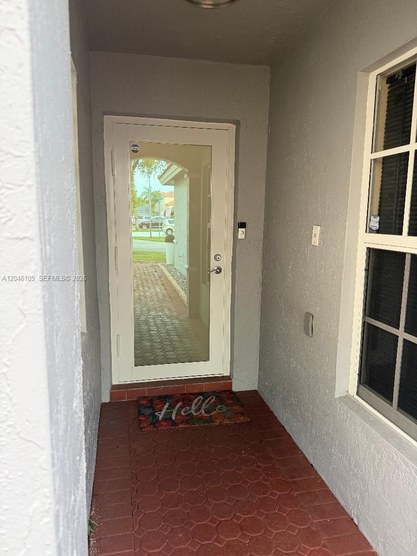 A front entryway features a glass-paneled door, a red brick floor, and a welcome mat — 19554 NW 79th Pl, Hialeah FL 33015, HIALEAH, FL