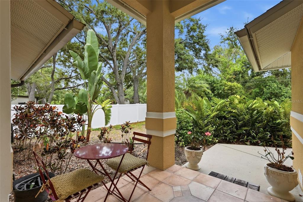 A covered patio features a small bistro table, two chairs, and views of a landscaped yard — 4989 162ND AVENUE N, CLEARWATER, FL