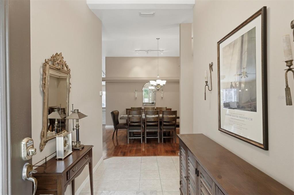 A foyer with tile flooring leads into a dining room with hardwood floors and furniture — 4989 162ND AVENUE N, CLEARWATER, FL