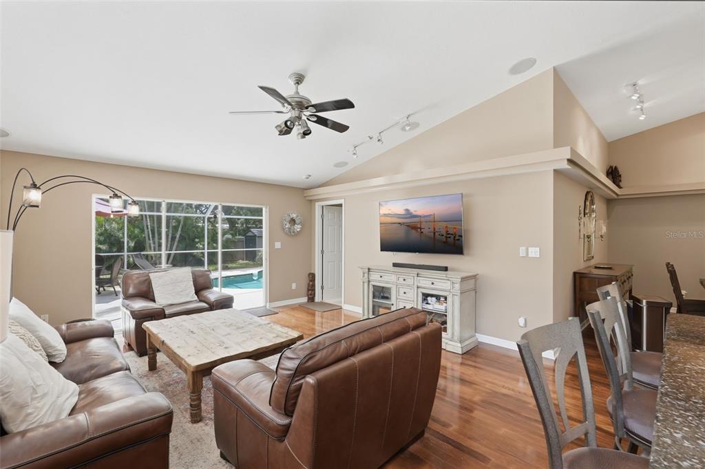 A living room with brown leather furniture, hardwood floors, a vaulted ceiling, and pool access — 4989 162ND AVENUE N, CLEARWATER, FL