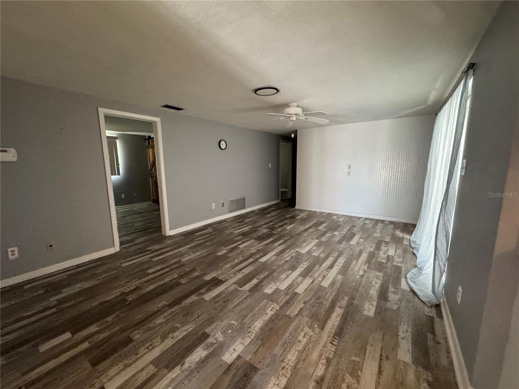 An empty living room features gray wood-look flooring, light gray walls, and a ceiling fan — 907 S FLORIDA AVENUE, TARPON SPRINGS, FL