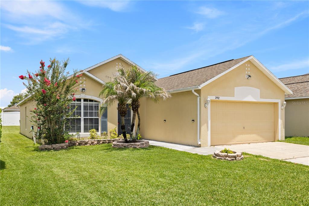 A single-story house with a tan stucco exterior, a two-car garage, and a front lawn — 2912 BELLE LANE, KISSIMMEE, FL