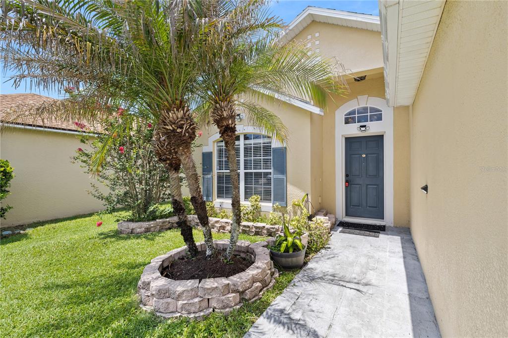 A front exterior view of a house with a palm tree and a stone planter — 2912 BELLE LANE, KISSIMMEE, FL