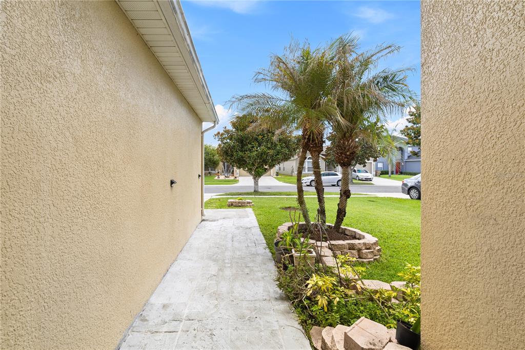 A paved walkway runs alongside a beige stucco house toward a front yard with palms — 2912 BELLE LANE, KISSIMMEE, FL