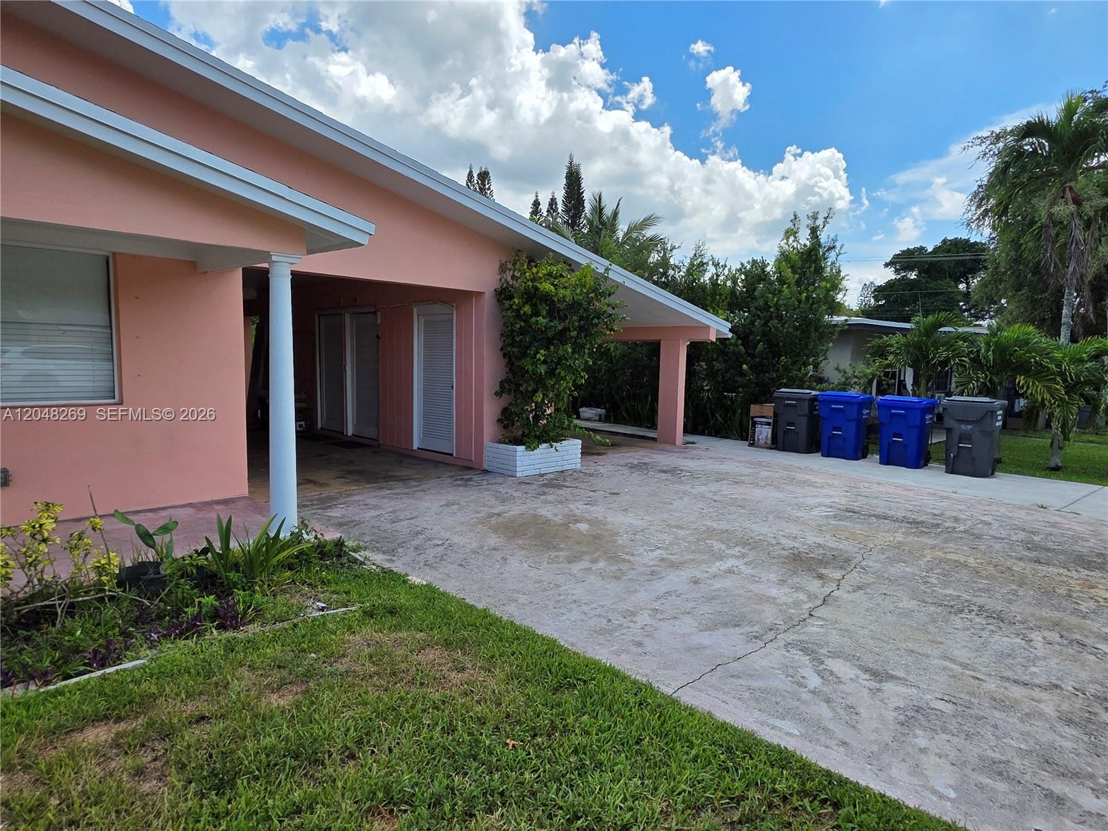 A pink house features a covered carport, a concrete driveway, and several outdoor trash bins — 6130 Funston St, Hollywood FL 33023, HOLLYWOOD, FL
