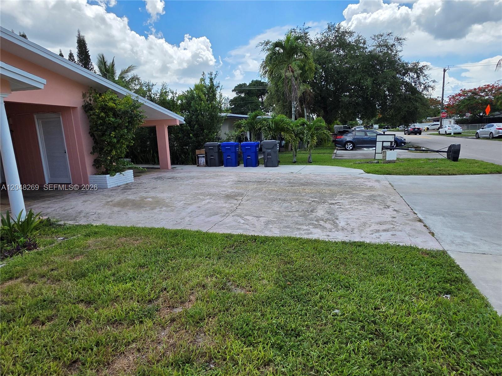 A pink house exterior features a concrete driveway, a covered entryway, and several trash bins — 6130 Funston St, Hollywood FL 33023, HOLLYWOOD, FL