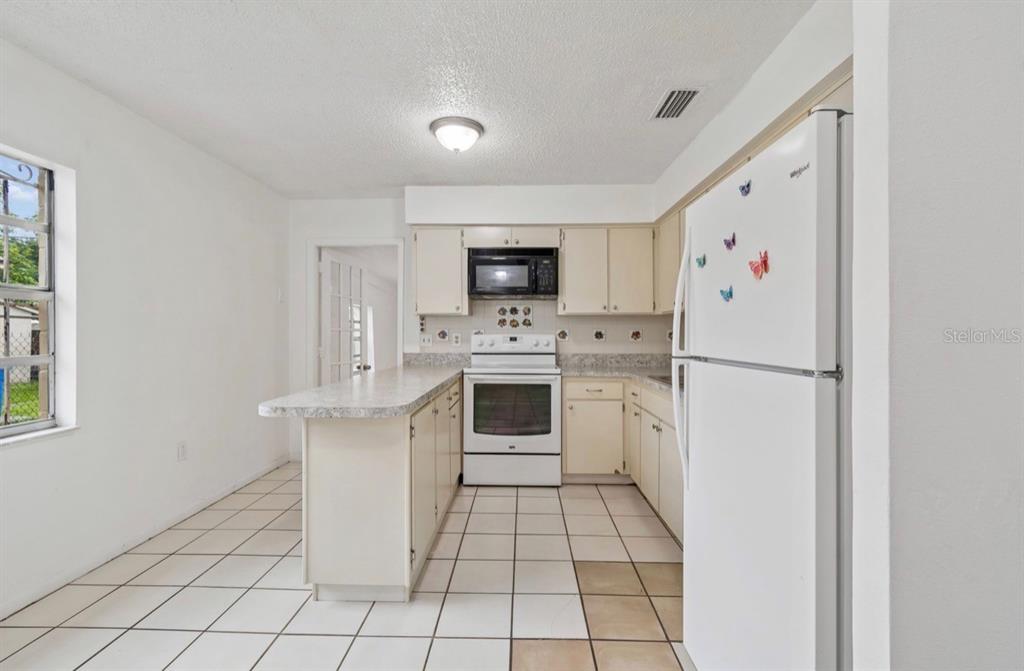 A kitchen features white appliances, light-colored cabinets, a peninsula, and white tile flooring — 7516 N CORTEZ STREET, TAMPA, FL