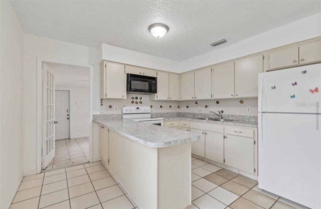 A kitchen with white cabinets, laminate countertops, a white refrigerator, and tiled flooring — 7516 N CORTEZ STREET, TAMPA, FL