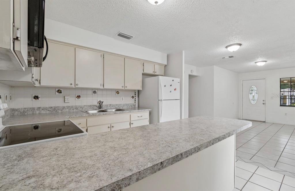 A kitchen with white cabinets, gray laminate countertops, and tile flooring, opening to an entryway — 7516 N CORTEZ STREET, TAMPA, FL