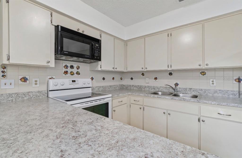 A kitchen features off-white cabinets, a black microwave, a white stove, and speckled laminate countertops — 7516 N CORTEZ STREET, TAMPA, FL