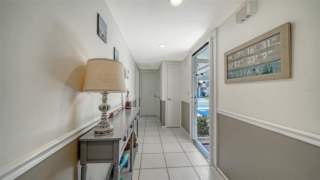 A hallway with white tile floors, a gray console table, and a Siesta Key sign — 2721 RIVERBLUFF PLACE UNIT V-50, SARASOTA, FL